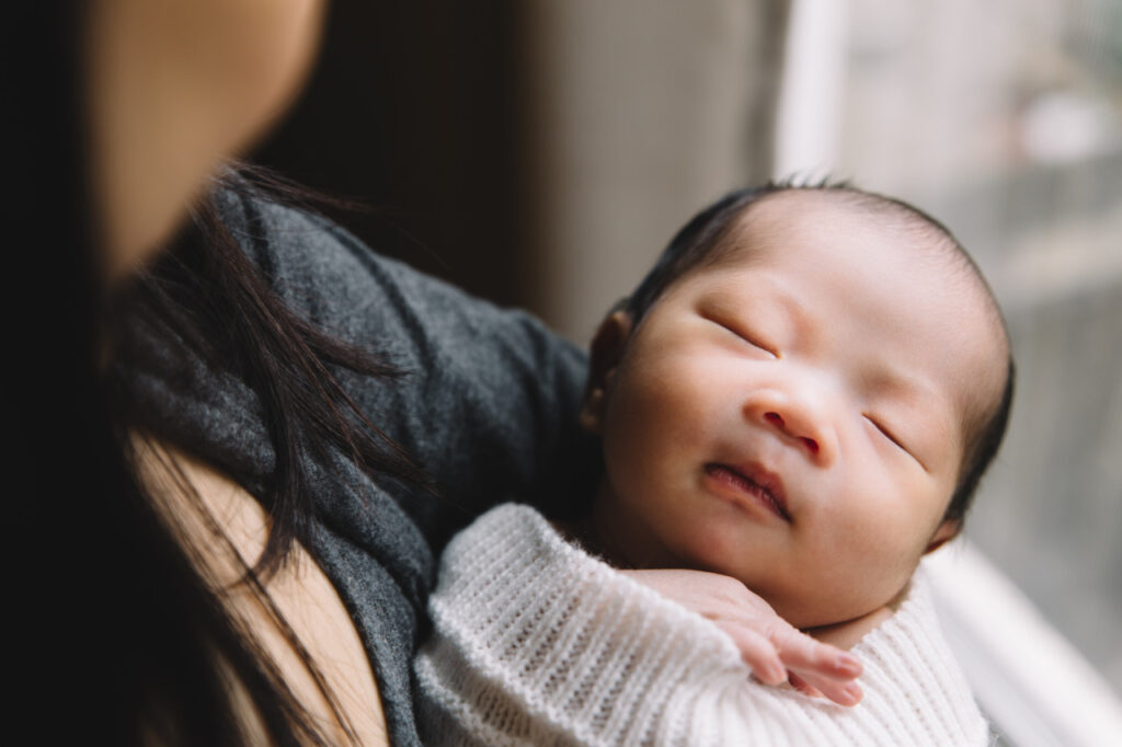 newborn baby is being held by mom near a window in the bedroom.