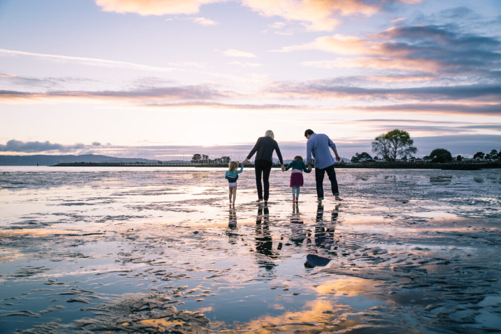 Family holding hands while wading in the shallow water at Crab Cove in Alameda.