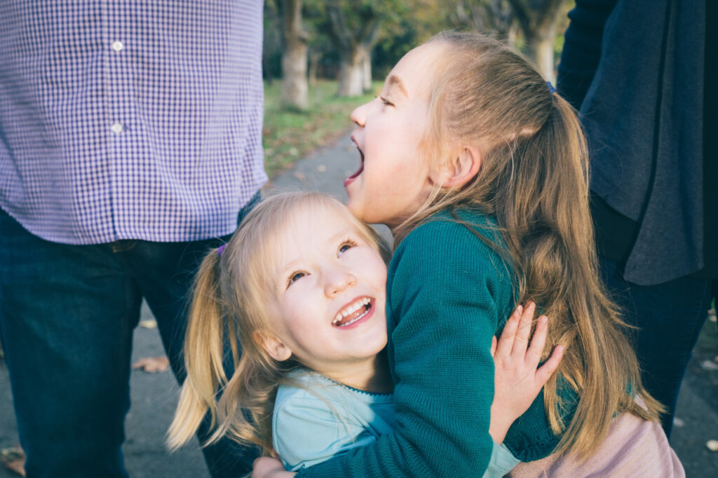 young sibling sisters laughing while hugging during a family photo session at Alameda Crown Beach.