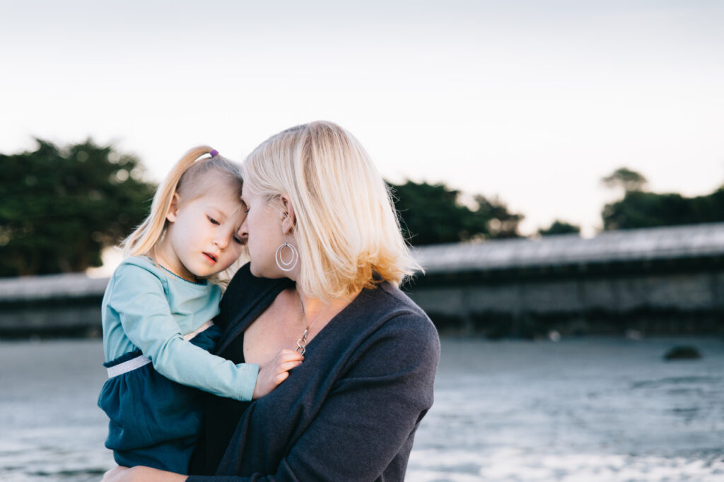 mother holding young toddler daughter while wading in the water at Crab Cove Beach Alameda.