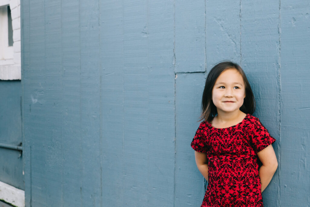 Toddler girl smiling while leaning against the boat house at Lake Merritt in Oakland.