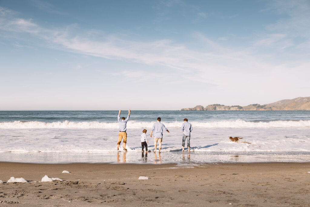 teenage boys laughing and jumping the waves at ocean beach in san francisco.