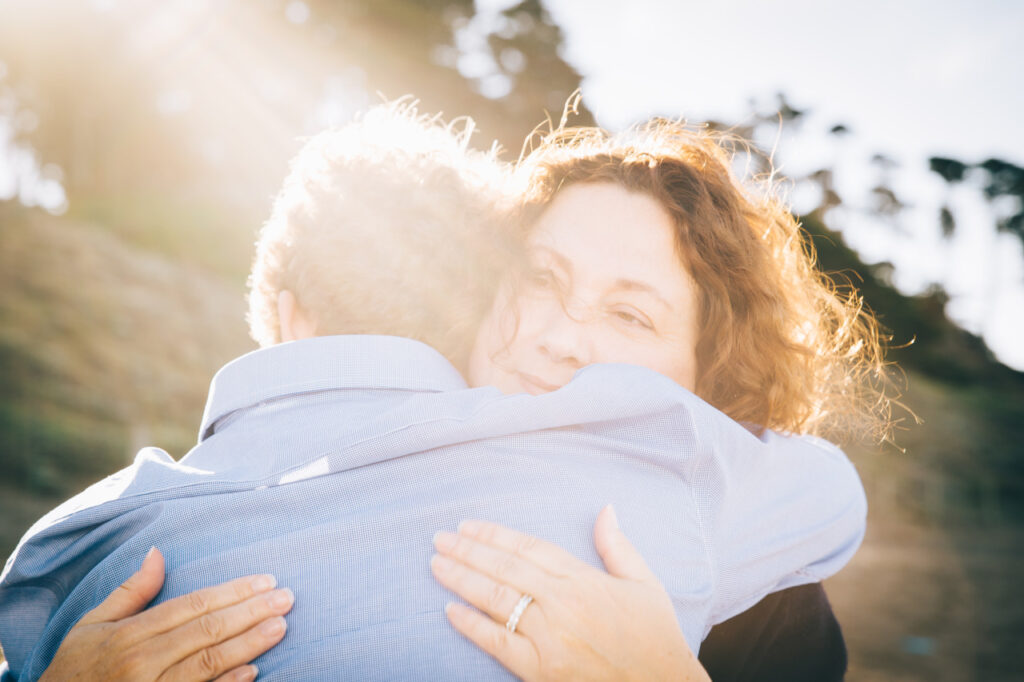 mother and teenage son hugging with sun flare at baker beach