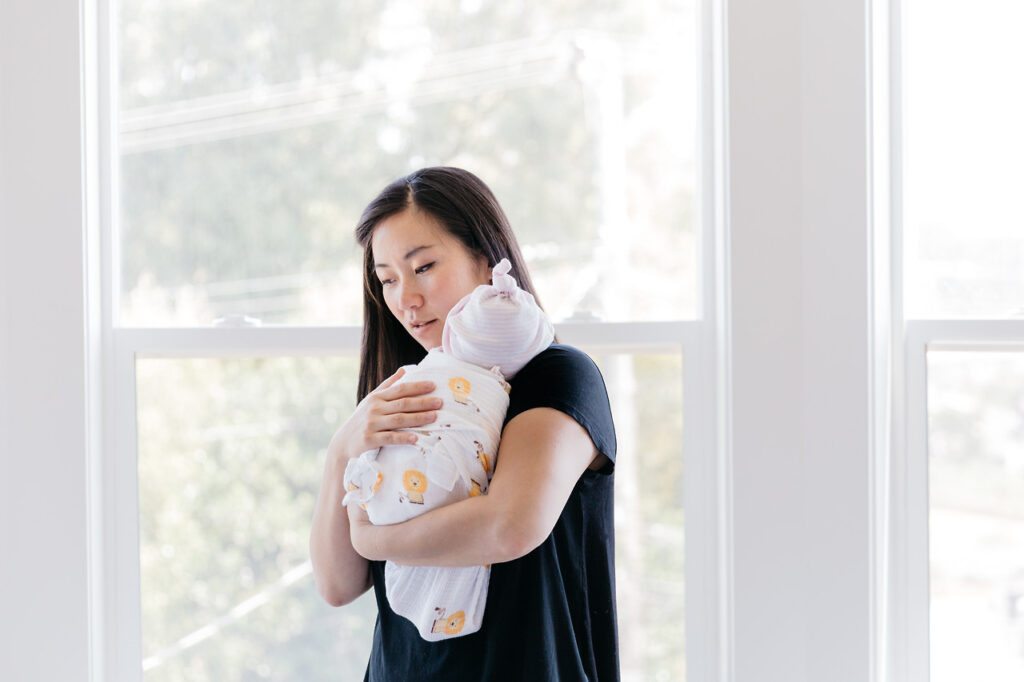 mother burping holding baby girl at window newborn home session sf bay area