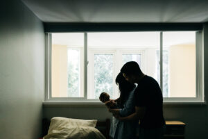silhouette portrait of family with baby newborn girl gazing up at mom and dad