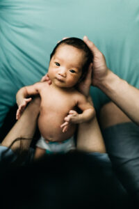 adorable newborn baby girl looking up at camera while mother holds her in her hands