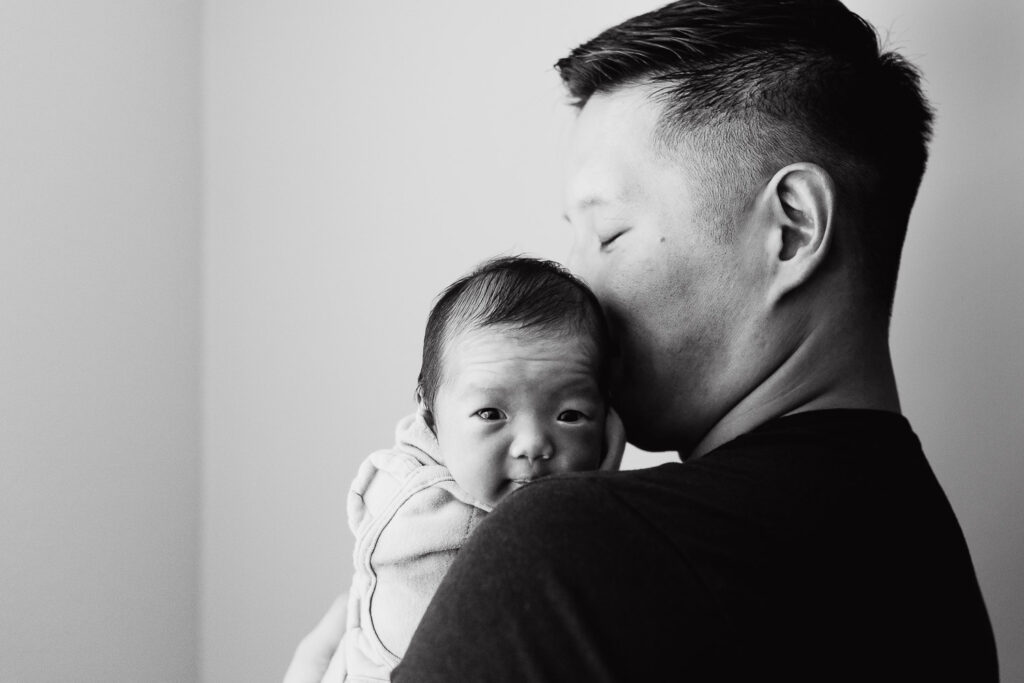monochrome portrait of father holding baby newborn girl with her peeking out on his shoulder