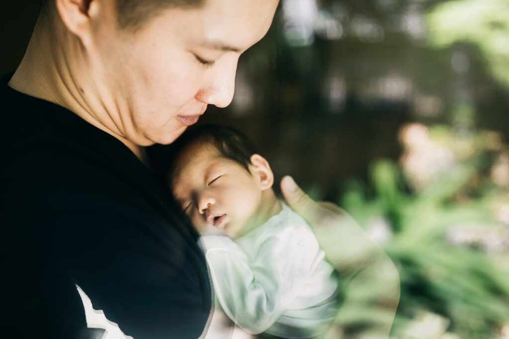 father holding baby newborn girl while she sleeps on his chest near window