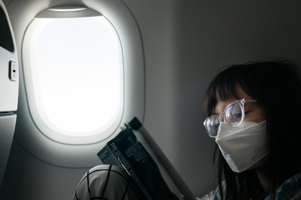 girl reading near window on hawaii airlines with face mask