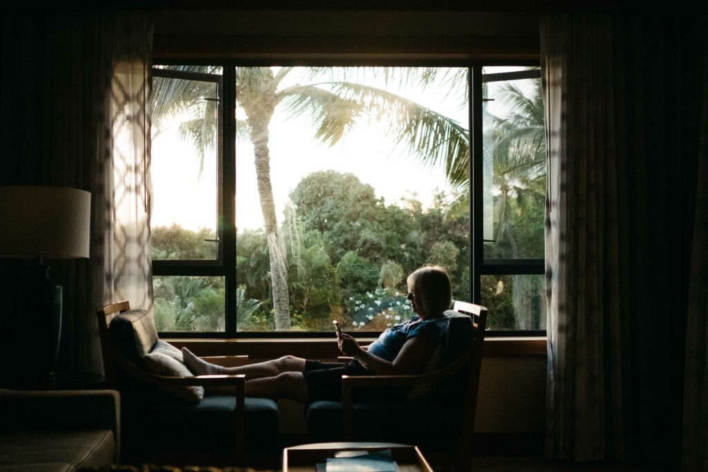 grandma reading her phone near window with palm trees outside in kauai