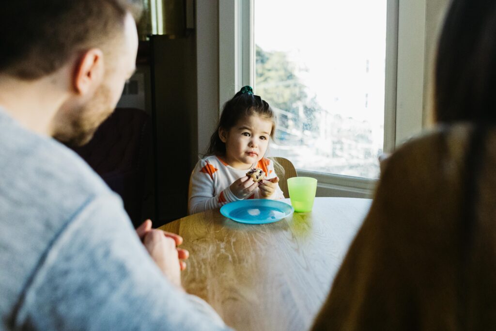 young girl being adorable and eating a muffin at the kitchen table