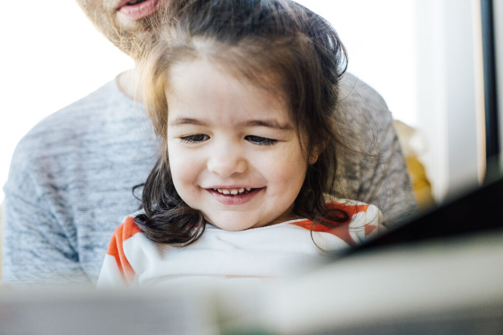 young girl smiling while dad is reading to her