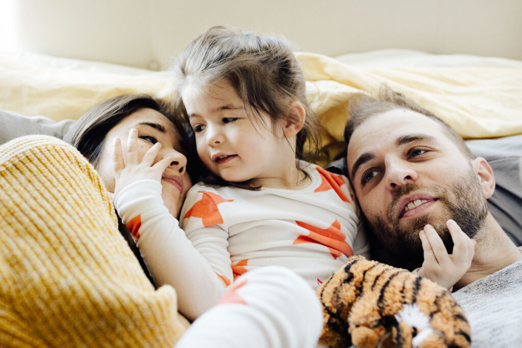 mom, dad, and daughter, being snuggly in the bed