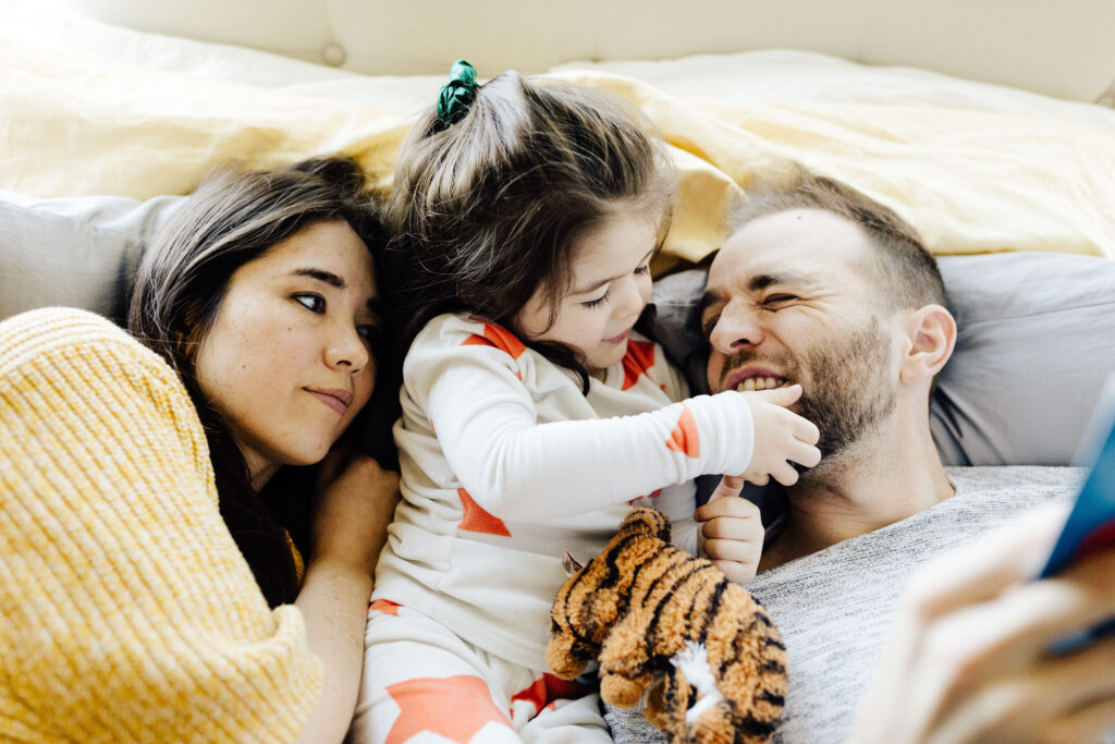 mom, dad, and daughter reading together in the bed and being snuggly
