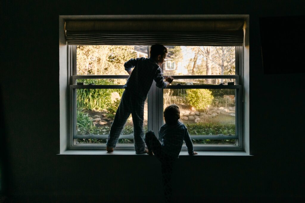 silhouette of sibling boys playing in the window with early morning light.