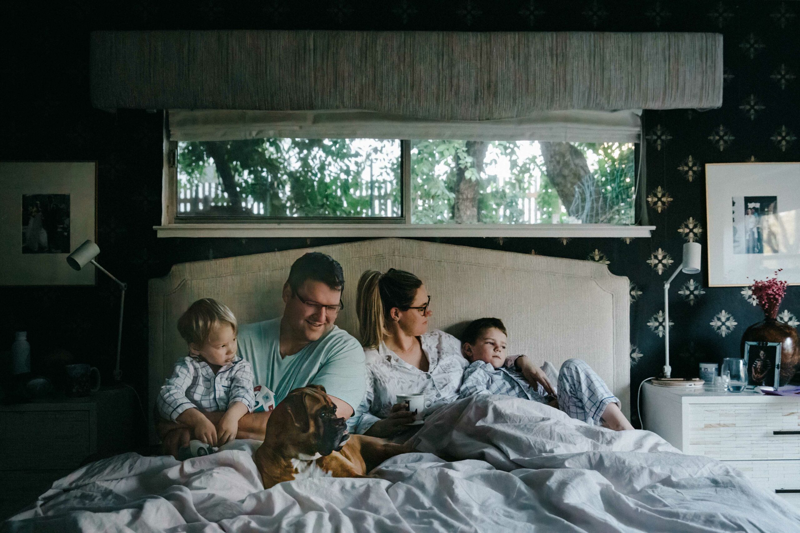 family snuggling in bed early in morning with dog.