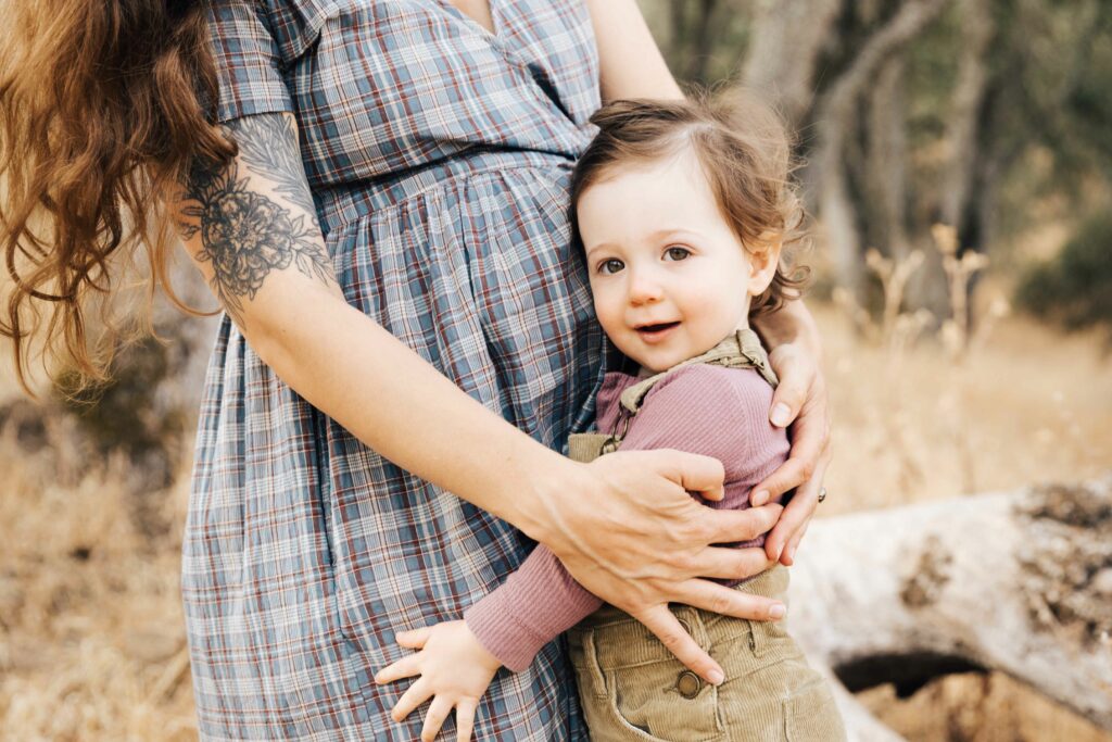 east-bay-family-photographer-IMG_0129-carmen-dunham-photography Young toddler girl holding mother's expecting belly in the meadow