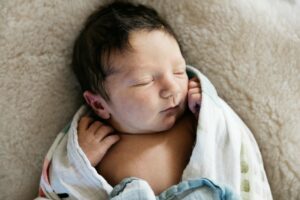 three day old baby sleeping in bed with loose swaddle