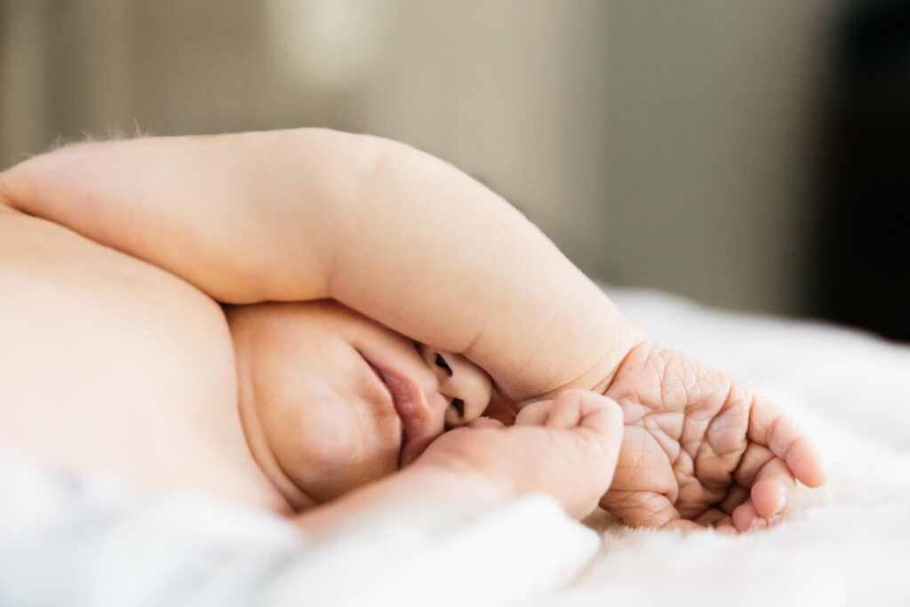 baby newborn covering his eyes while he sleeps on parents' bed
