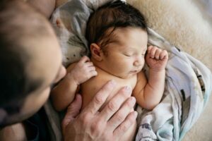 three day old newborn with father's hands resting on his chest