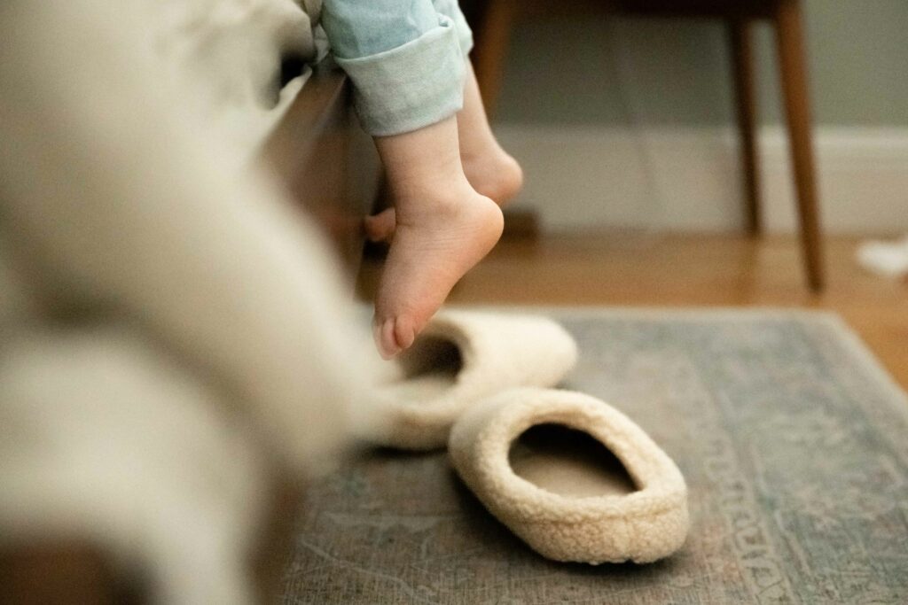 toddler toes dangling from the bedside as she tries to climb onto the bed