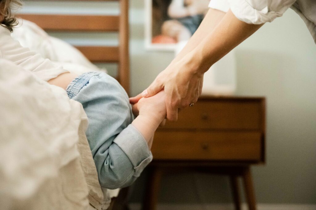 mom holding toddler daughter's feet as she tries to climb on the bed