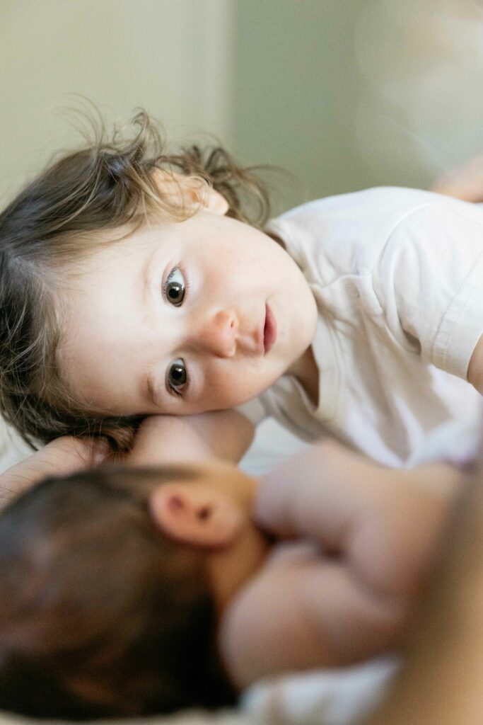 young toddler sister admiring younger baby brother in the bed during newborn photo session