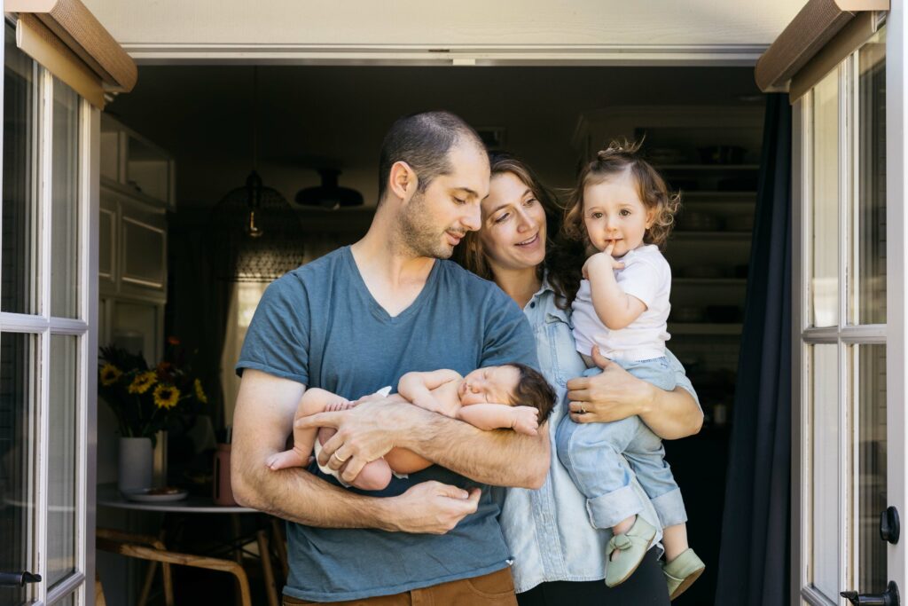 family of four posing at home with new baby
