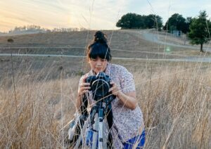 woman adjusting camera on tripod in a field of tall grass