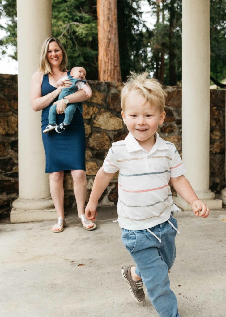 Young boy running around the columns at the Morcom Rose Garden while mom watches from afar