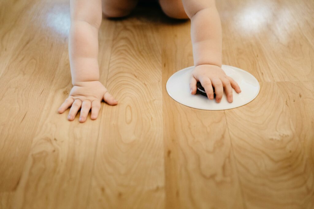 Toddler boy playfully pushing an Orea cookie around the kitchen floor.