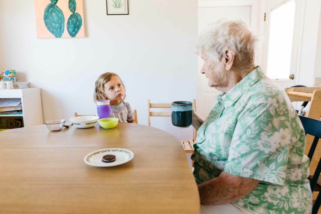 Grandma and toddler grandson having a conversation at the kitchen table during snack time.