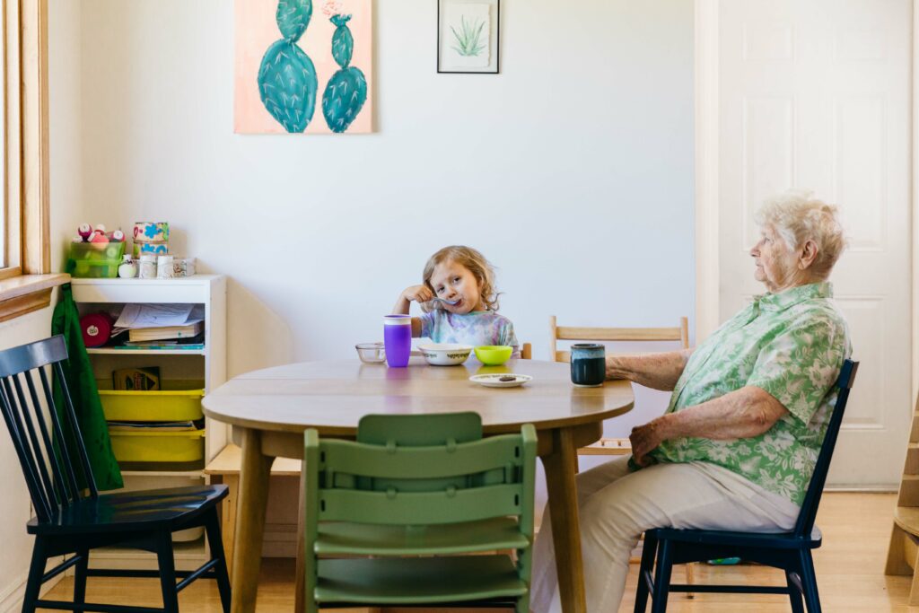 Grandma and toddler grandson having a snack on the kitchen table.