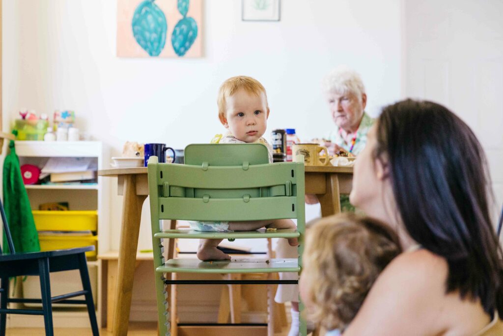 Toddler boy exchanging glances with mom and older brother at the kitchen table.