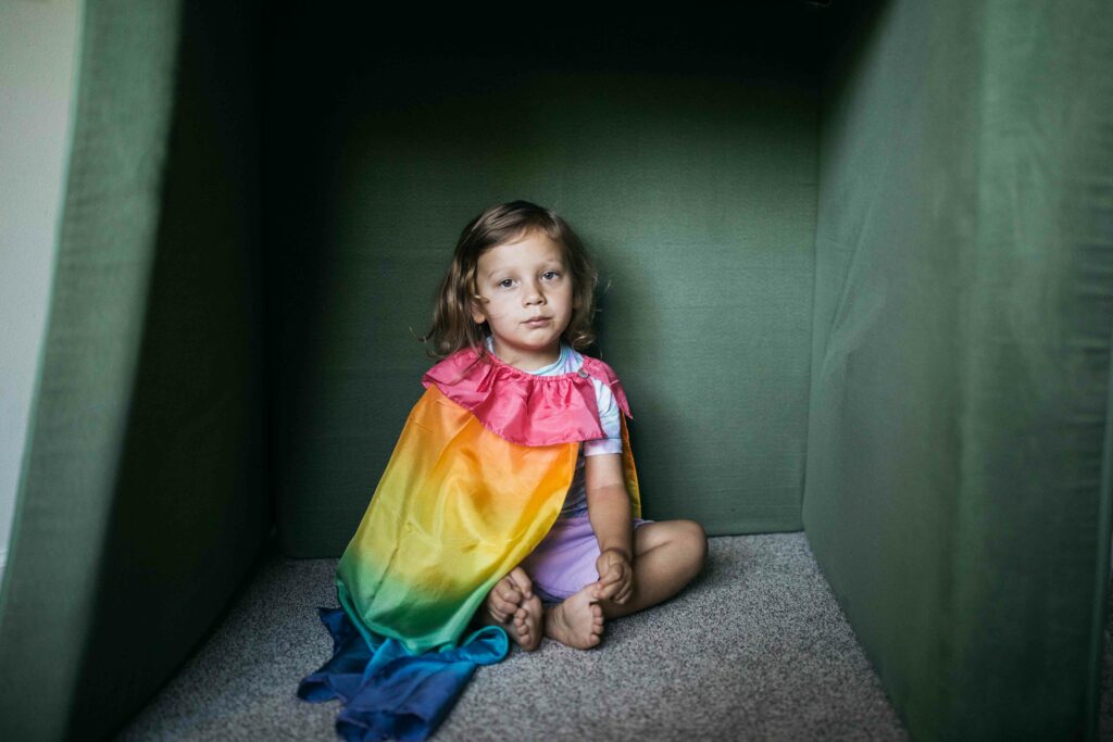 toddler boy in a rainbow cape in his play room