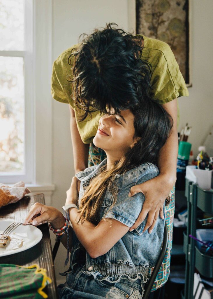 Mother and tween daughter bonding at the kitchen table.