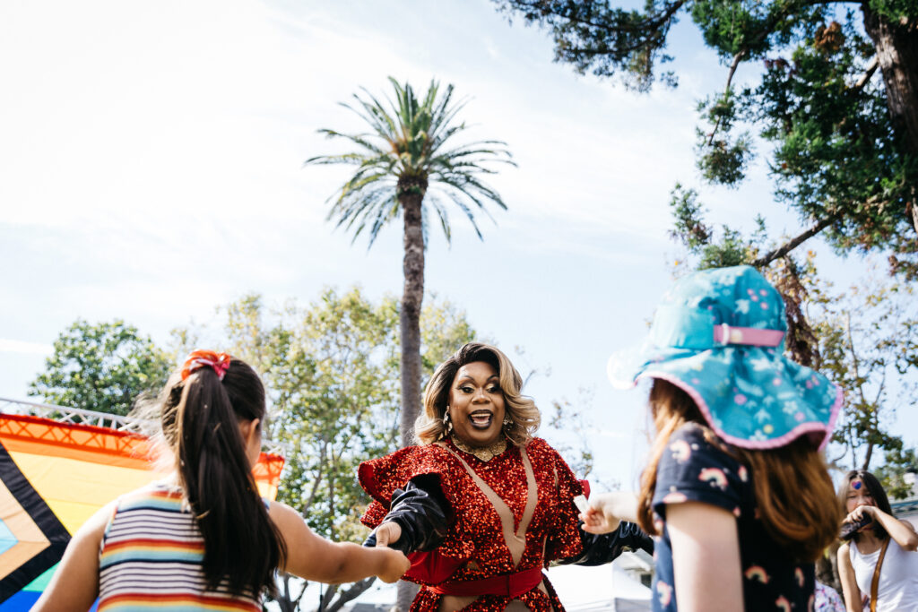 Drag diva jumping in the air performing at Alameda Pride with young spectators