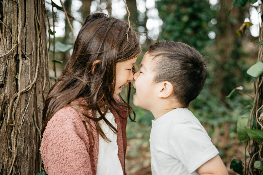 Brother and sister sharing a nose kiss among the eucalyptus trees in the Presidio.