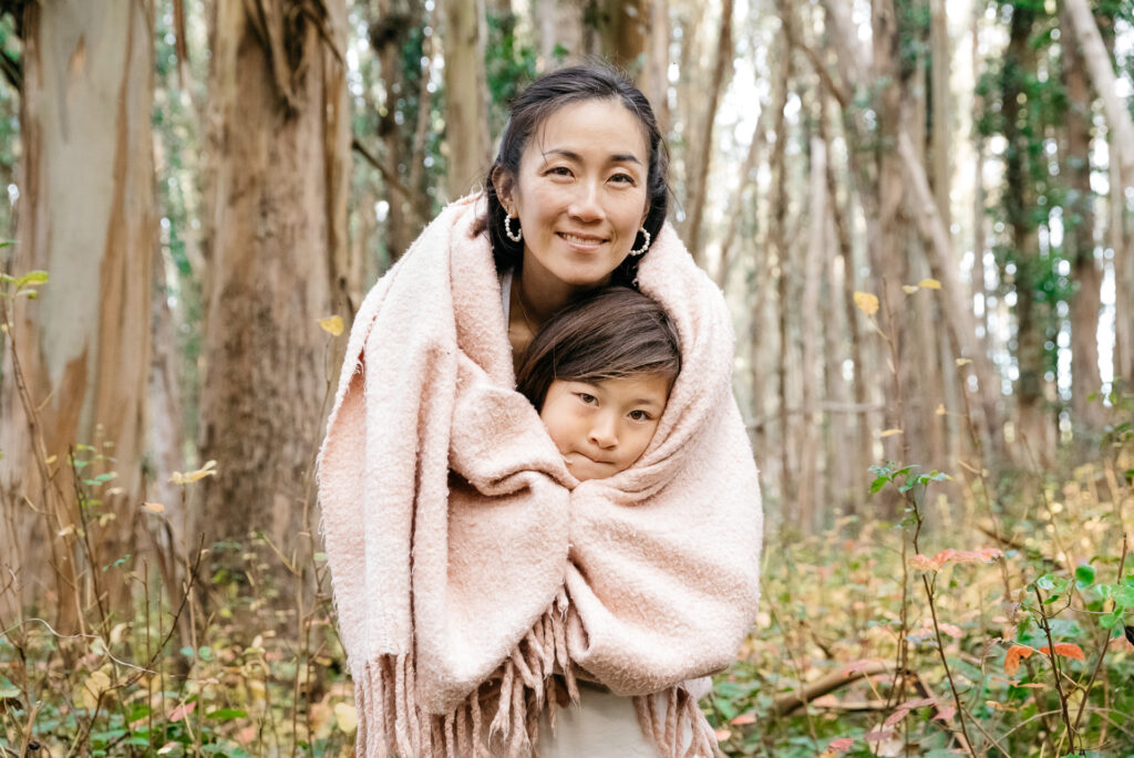 Mom wrapping young daughter in a blanket in the Presidio during a family photo session.