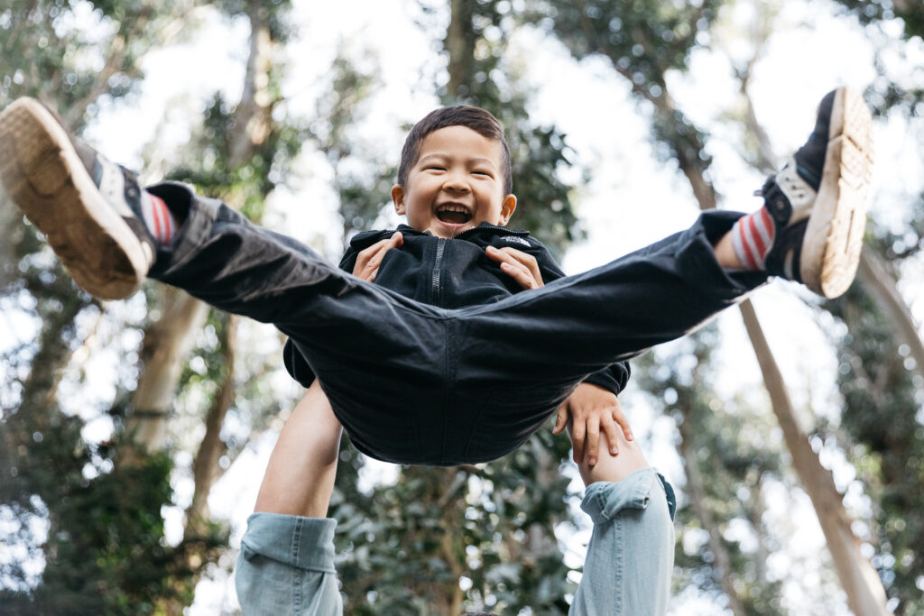Young son is laughing while his father is throwing him in the air during a family photo session.