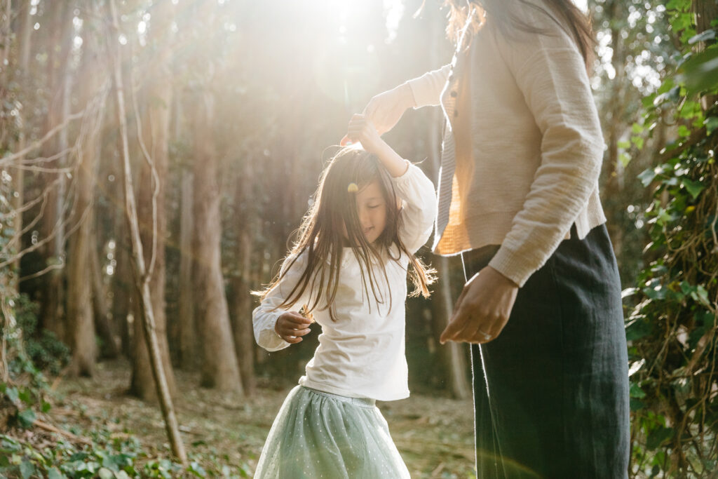 Mother is twirling young daughter as she dances during a family photo session at Andy Goldsworthy Wood Line.