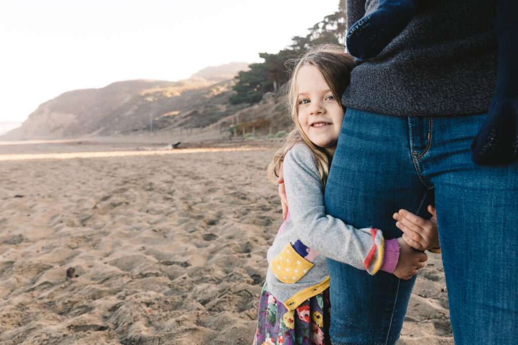 young girl hugging mom's leg during a family photo session at baker beach.