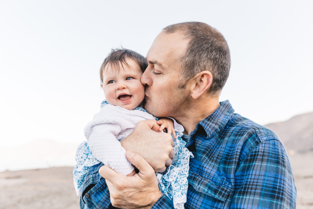 dad kissing and holding young daughter at baker beach.