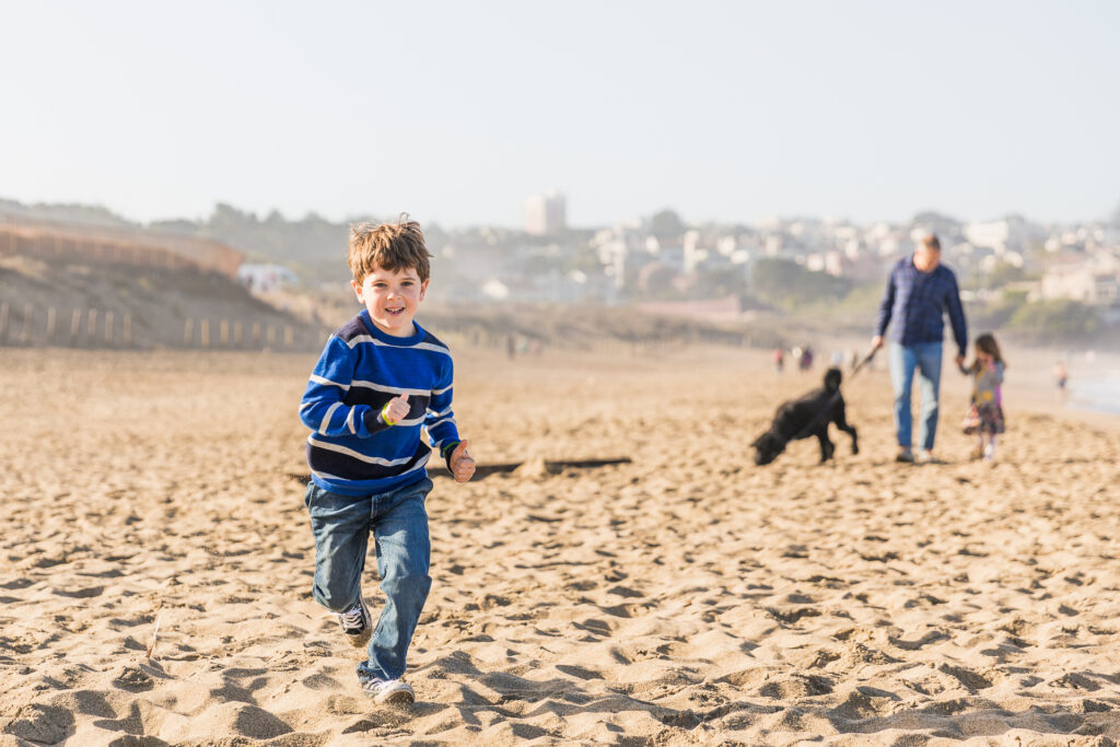 young son running in the sand at baker beach.