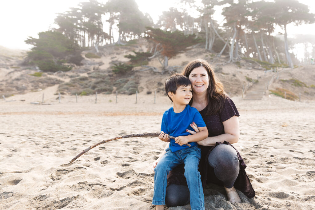 young boy sitting on his mom's lap in the sand at baker beach.