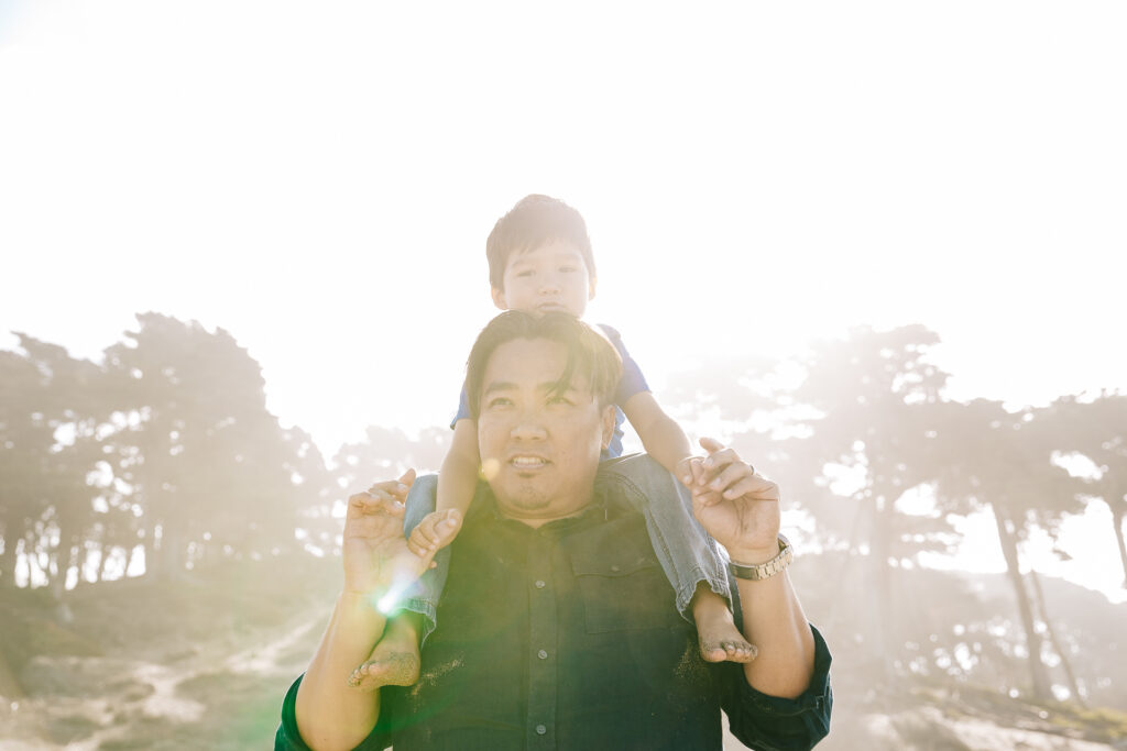 dad carrying young son on his shoulders at baker beach during a family photo session in san francisco.