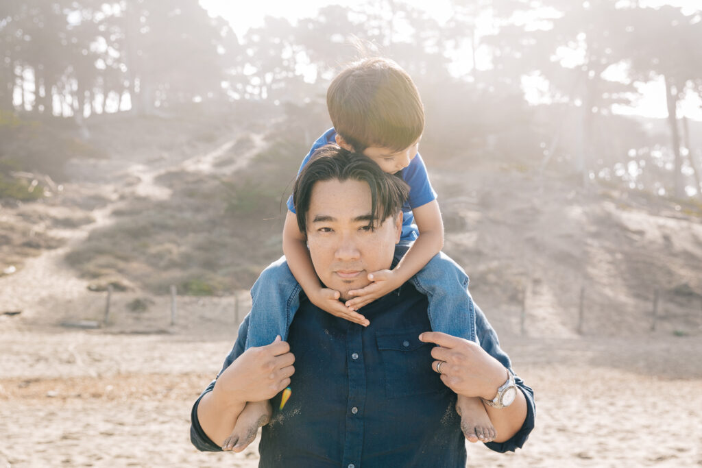 dad carrying young son on his shoulders at baker beach.