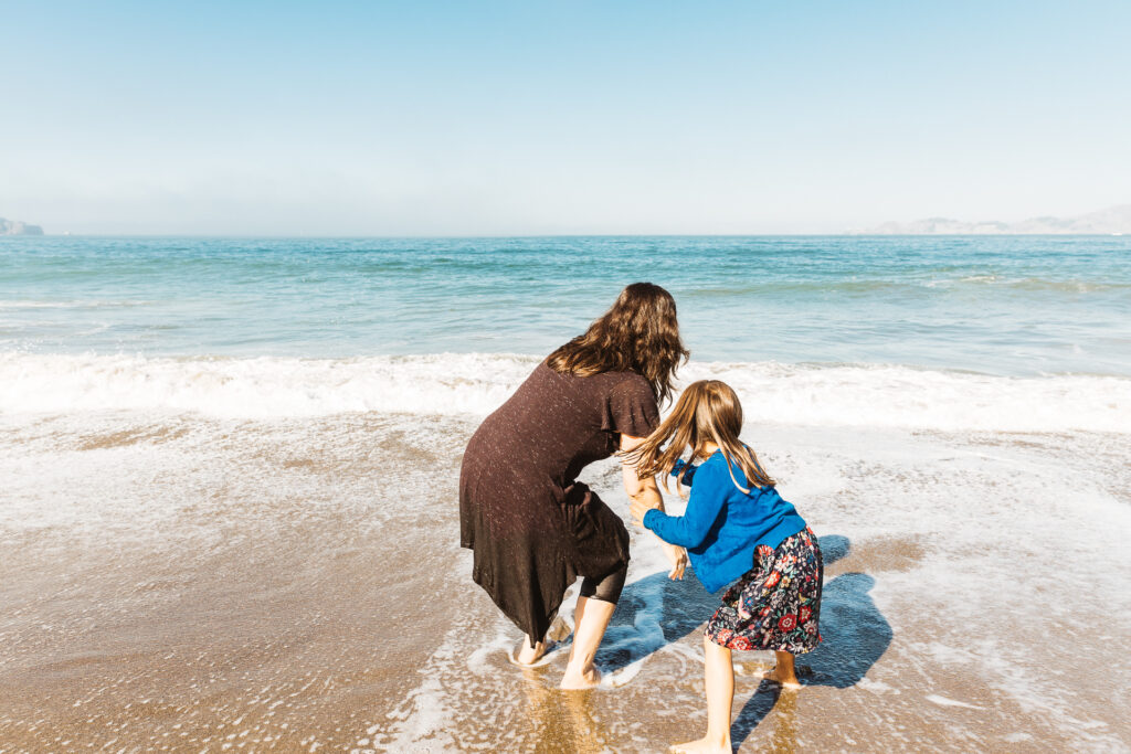 mom and daughter chasing the waves at baker beach during a family photo session.