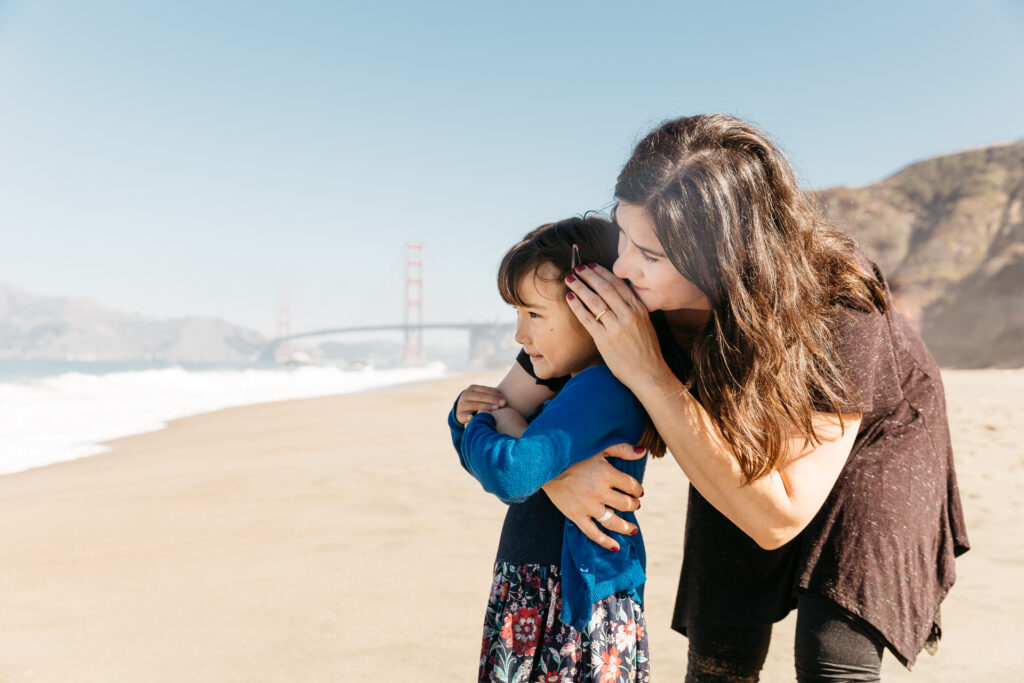 mom tenderly holding daughter at baker beach during a family photo session.