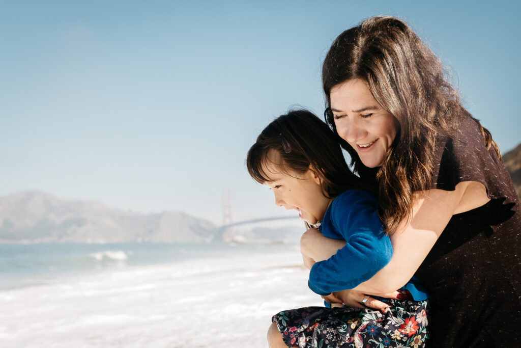 mom holding daughter while she jumps the wave at baker beach.